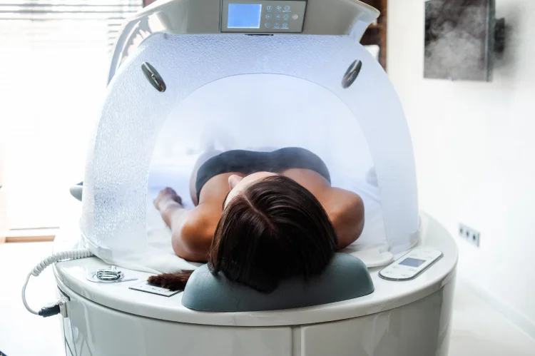 A person lying inside a wellness treatment capsule with a control panel