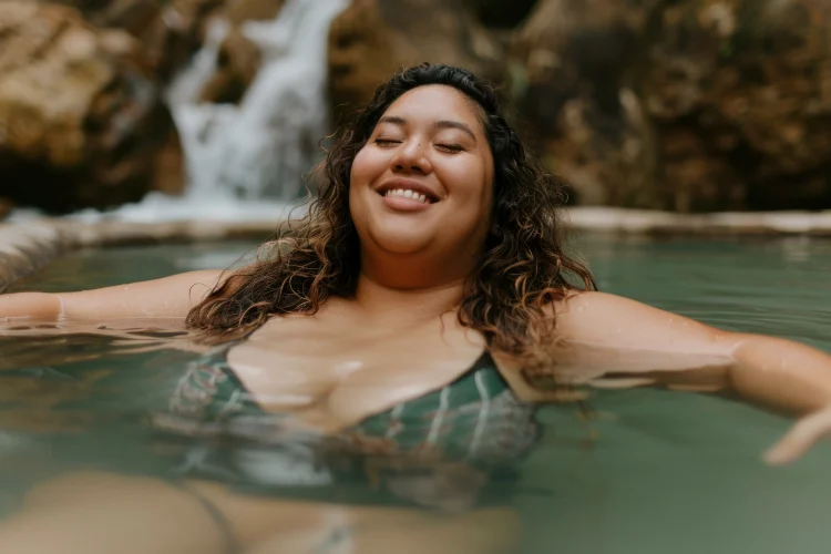 A woman relaxing in a natural thermal pool beneath a waterfall